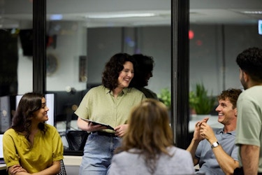 A group of young entrepreneurs are gathered around an office table as they laugh and talk.