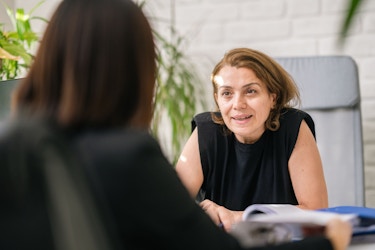 A woman office manager talks to another woman, whose face is not visible in the image. 