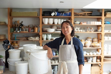 A woman ceramicist leans against a tub in her work studio.