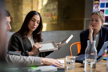 Men and women business colleagues discuss a product's packaging. A woman holds up a protoype box while the team discusses it.
