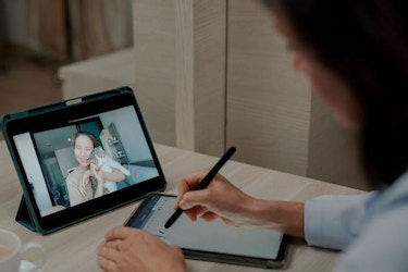 A young female cat owner is pictured on a tablet screen talking to a woman veterinarian about the condition of her cat.