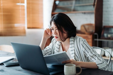  A young woman who looks concerned reviews financial information using a laptop computer. 